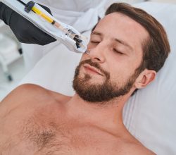 Man lying with his eyes shut during the skin rejuvenation procedure performed by a cosmetician